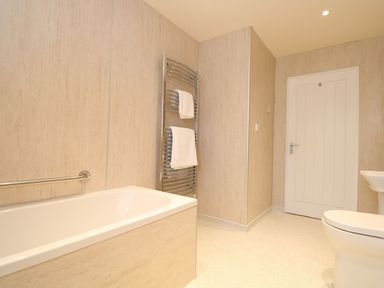 A bathroom with a bathtub, towel rack, towels, and toilet at Elm Cottage in Truro