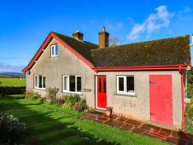 A house with a red door and windows surrounded by grass and flowers at The Bungalow in Penrith