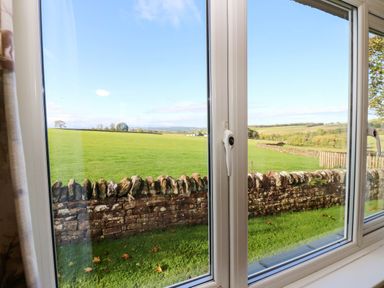 A view from a window showing grass and a stone wall at The Bungalow in Penrith