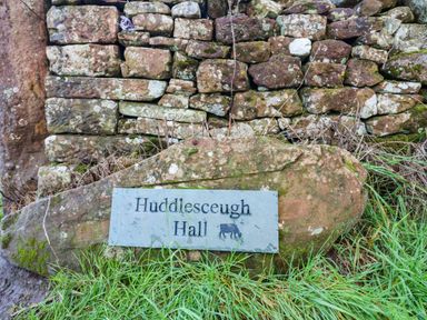 A sign reading Huddisceugh Hall next to a stone wall and grass