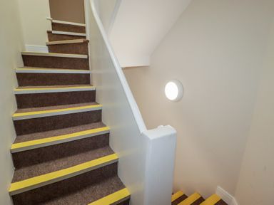 A staircase with carpeted steps and a light fixture at Flat 5 Tenby
