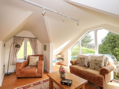 A snug with a sofa and chair beside a window at High Beck Cottage in Kendal