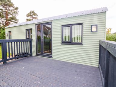 An outdoor view of a cabin with a deck and multiple windows at Calendonia Hut West Mains near Haggerston