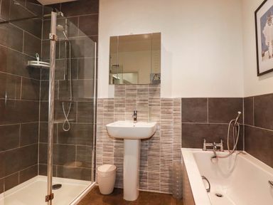 A bathroom with a shower, bathtub, sink and mirror at Apartment 1 in Newquay