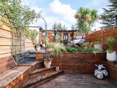 A garden with wooden deck, plants, and a hanging chair at Severnwolf House in Gloucester