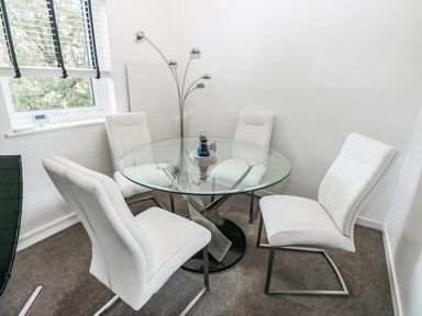 A dining room with a glass table and white chairs at 21 Ferrara Square in Swansea