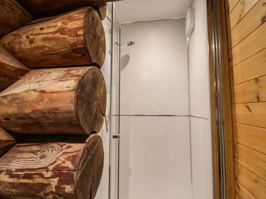 A bathroom with wooden logs, a shower glass door, and paneling at Thimble Lodge in Gunnislake