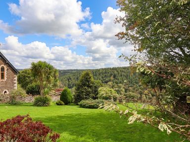 A garden with trees and a house at Thimble Lodge in Gunnislake