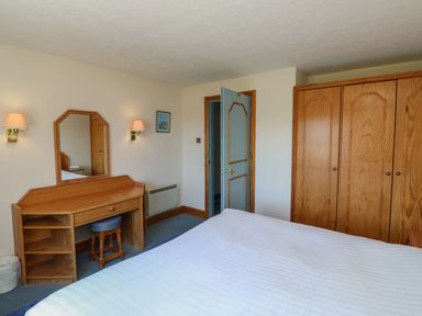A bedroom with a bed, wardrobe, and dressing table at Nightjar in Kingsteignton