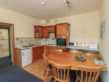 A kitchen with wooden cabinets and a dining table at Egret in Kingsteignton