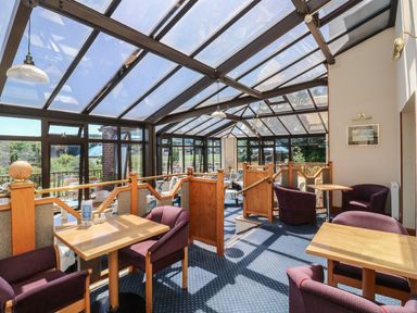 A conservatory with wooden tables and chairs at Egret in Kingsteignton