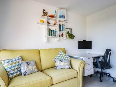 A living room with a yellow sofa and a desk with a computer monitor at Harber Rise in Carlyon Bay