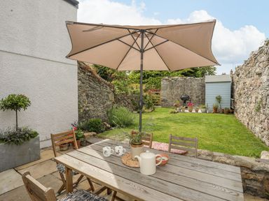 A garden with a table and chairs under an umbrella at Swn y Mor (Wexham) Beaumaris