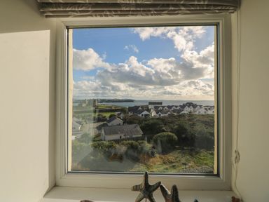 A view from a window showing a landscape with houses and the sea at Llywelyn in Trearddur Bay