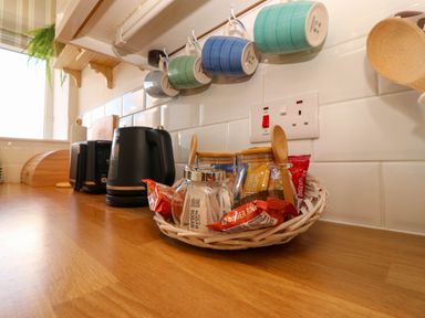 A kitchen counter with kettle, cups, sugar jar, and biscuits at Llywelyn in Trearddur Bay