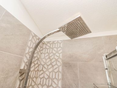 A shower head and tiled wall in a bathroom at Thirlmere Scar Troutbeck Bridge