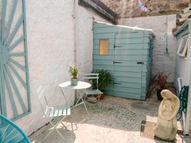 A garden with a shed, table, chairs, and plants in a courtyard