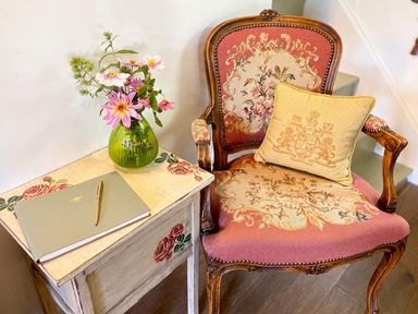 A sitting room with an armchair and a table holding flowers and a notebook
