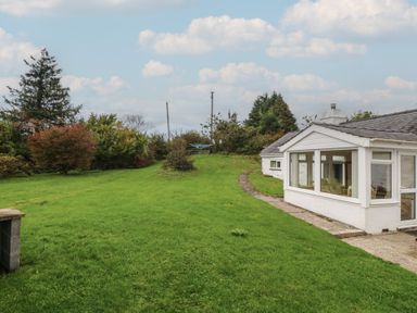 An outdoor view of a house surrounded by grass and trees at Bryn Eithin in Penygroes