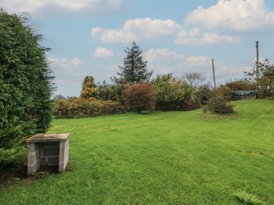 A garden with a stone table and trees at Bryn Eithin in Penygroes