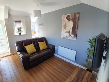 A living room with a sofa, lamp, plant, and artwork at 1 Bedroom Apartment with Sea View, Mevagissey