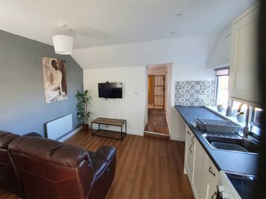 A living room with a sofa, television, and kitchen countertop at 1 Bedroom Apartment with Sea View Mevagissey