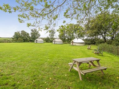 An outdoor area with yurts, a picnic table, and chairs at Yurt, Sleeps 2 with BBQ and Fire Pit, Tregooden Farm near St Tudy