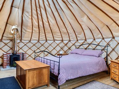 A bedroom in a yurt with a bed and a wood stove at Yurt, Sleeps 2 with BBQ and Fire Pit, Tregooden Farm near St Tudy