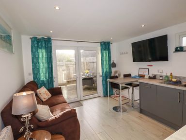 A living room with a sofa and kitchen area at The Old Dairy in Wadebridge