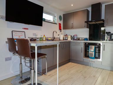 A kitchen with a television, bar stools, and an oven at The Old Dairy in Wadebridge