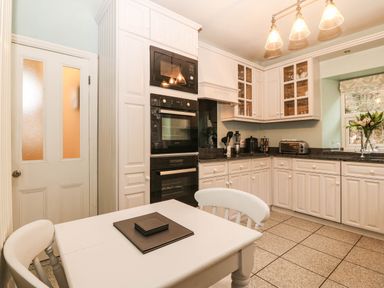 A kitchen with cabinets, countertop, table, and appliances at Craig Y Glyn