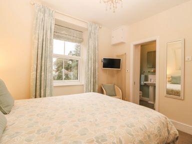 A bedroom with a bed, curtains, television, and an en-suite bathroom at Craig Y Glyn