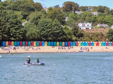 A beach with beach huts and people enjoying activities at Craig Y Glyn Cottage in Pwllheli