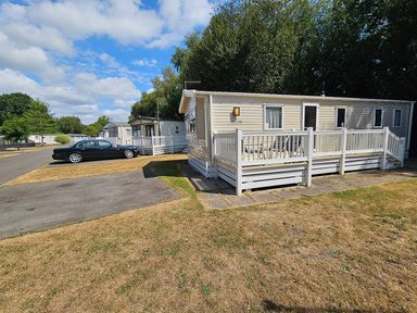 A mobile home with a car parked nearby at a holiday park