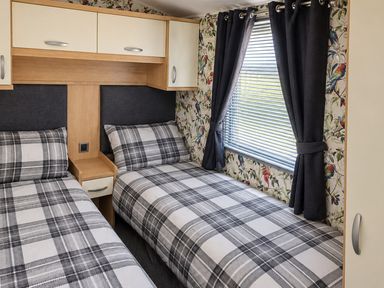 A bedroom with two single beds and curtains at 3 Bedroom Seafront Caravan, Sleeps 6 with Parking