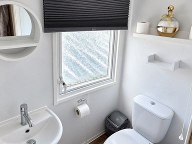 A bathroom with a sink, toilet, and window at 3 Bedroom Seafront Caravan, Sleeps 6 with Parking