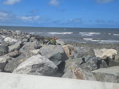 A rocky beach with boats in the distance and a blue sky at the coast