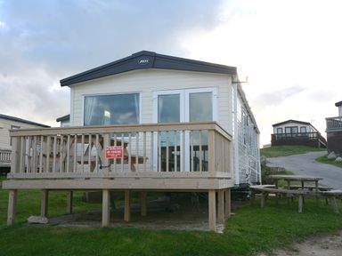 A mobile home with a deck and sign at Perran Sands Holiday Park - 615 Chy-an-Mor Perranporth