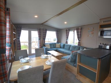 A living room with a sofa and dining area at Perran Sands Holiday Park - 615 Chy-an-Mor Perranporth