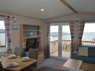 A living room with a television and balcony view at Perran Sands Holiday Park - 615 Chy-an-Mor Perranporth