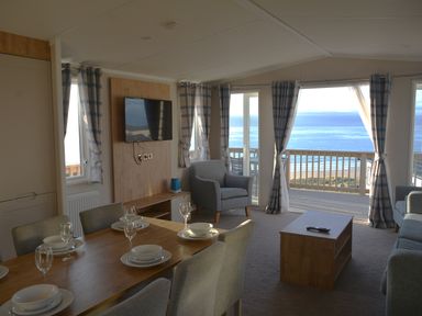 A living room with a dining table and large windows at Perran Sands Holiday Park - 621 Chy-an-Mor Perranporth