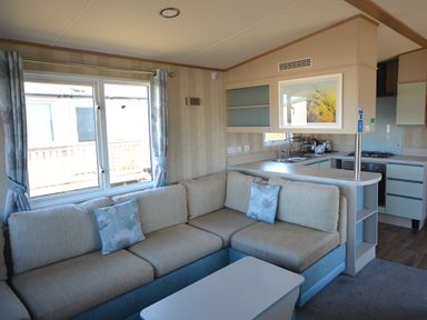 A living room with a sofa and kitchenette at Perran Sands Holiday Park - 725 Kernow View Perranporth