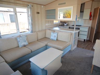 A living room with a sofa and kitchen area at Perran Sands Holiday Park - 725 Kernow View, Perranporth