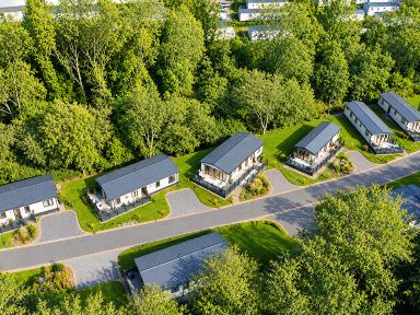 A row of holiday homes surrounded by trees and grass at Hoburne Devon Bay - Woodland Glade 24 Paignton