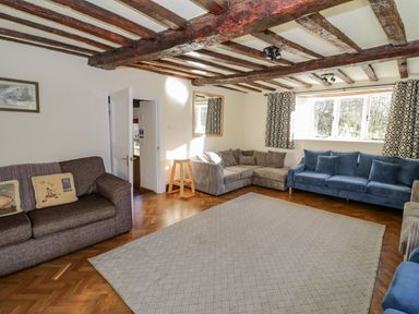 A living room with brown and blue sofas wooden beams on the ceiling and a large window at Little Cowarne Court Little Cowarne near Bromyard