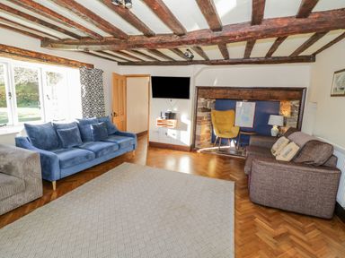 A living room with wooden ceiling beams blue and brown sofas a yellow chair and a wall-mounted television at Little Cowarne Court in Little Cowarne near Bromyard