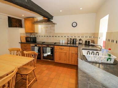 A kitchen with wooden cabinets a dining table and chairs black countertop and appliances at Little Cowarne Court Little Cowarne near Bromyard