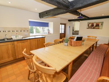 A dining area with a long wooden table surrounded by wooden chairs and a bench with a cushion at Little Cowarne Court in Little Cowarne near Bromyard