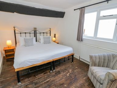 A bedroom with a double bed two bedside tables with lamps a striped armchair and a window at Little Cowarne Court Little Cowarne near Bromyard