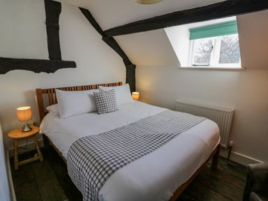 A bedroom with a wooden bed a bedside table with a lamp and a window at Little Cowarne Court in Little Cowarne near Bromyard
